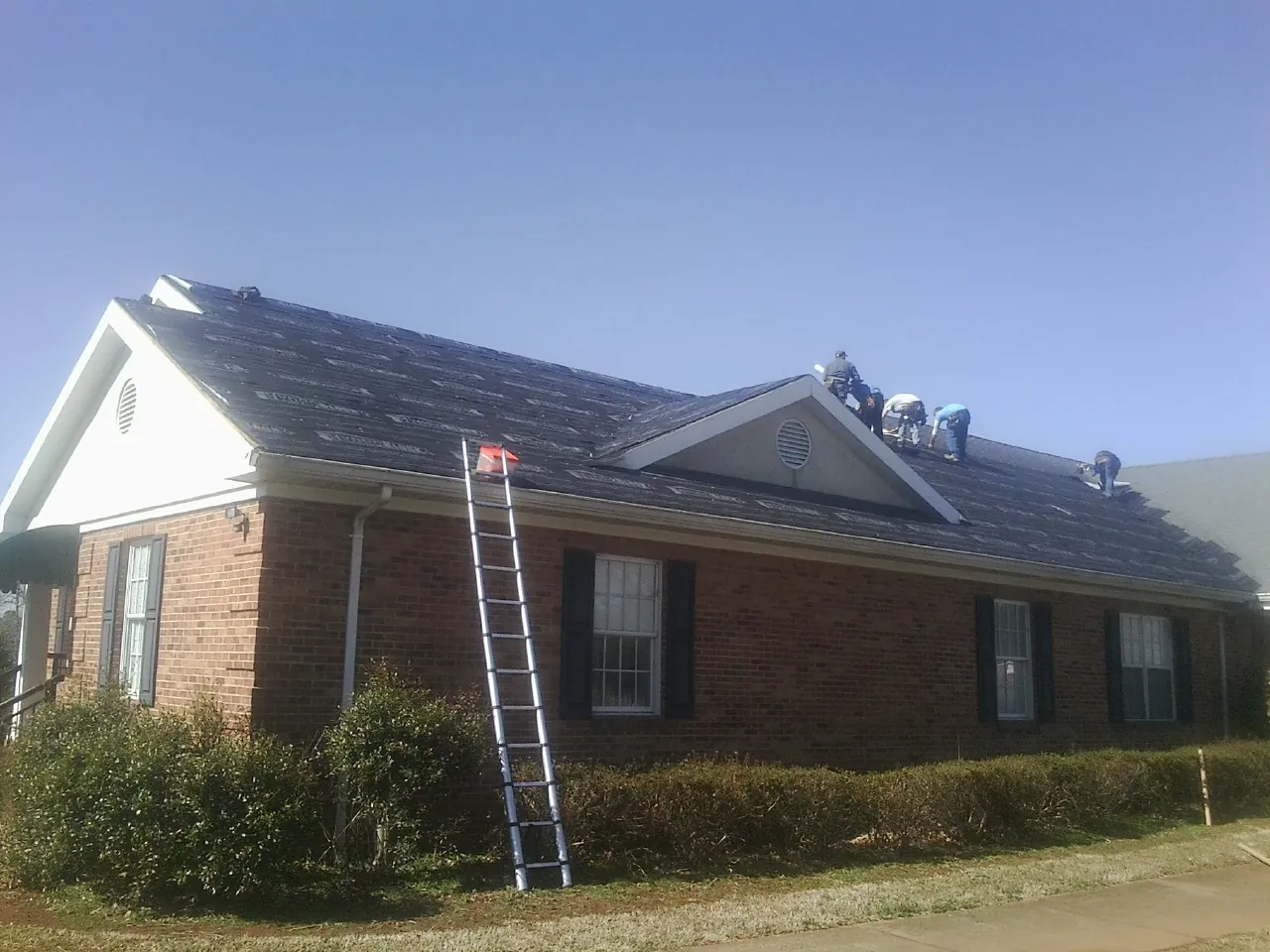 Crew tearing shingles off a brick ranch roof with a ladder set — Emergency Roof Repair work by our crew in Bound Brook