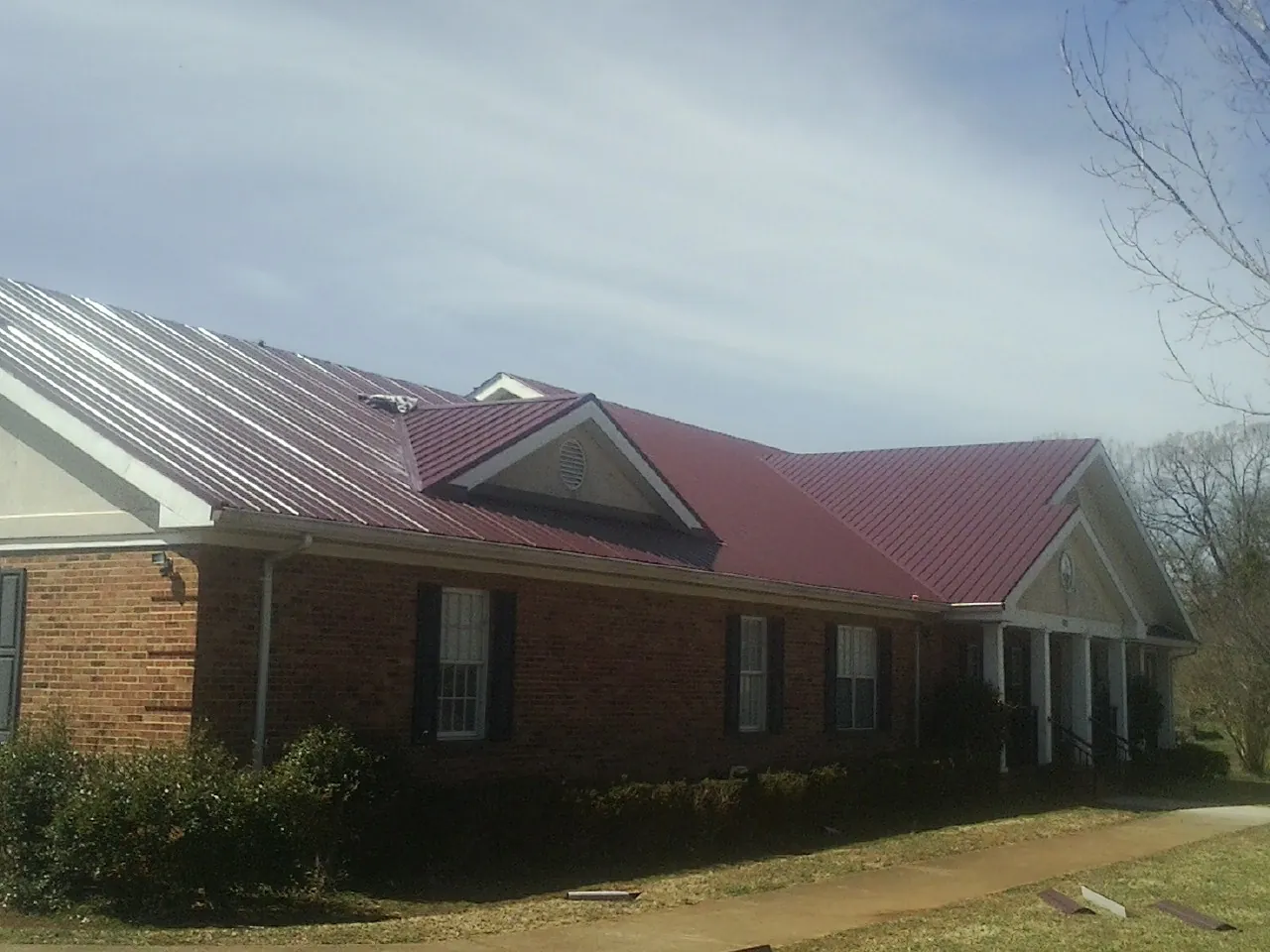 Red metal roof with gabled entries on a long brick building, from a Hail Damage Roof Repair job in Bound Brook
