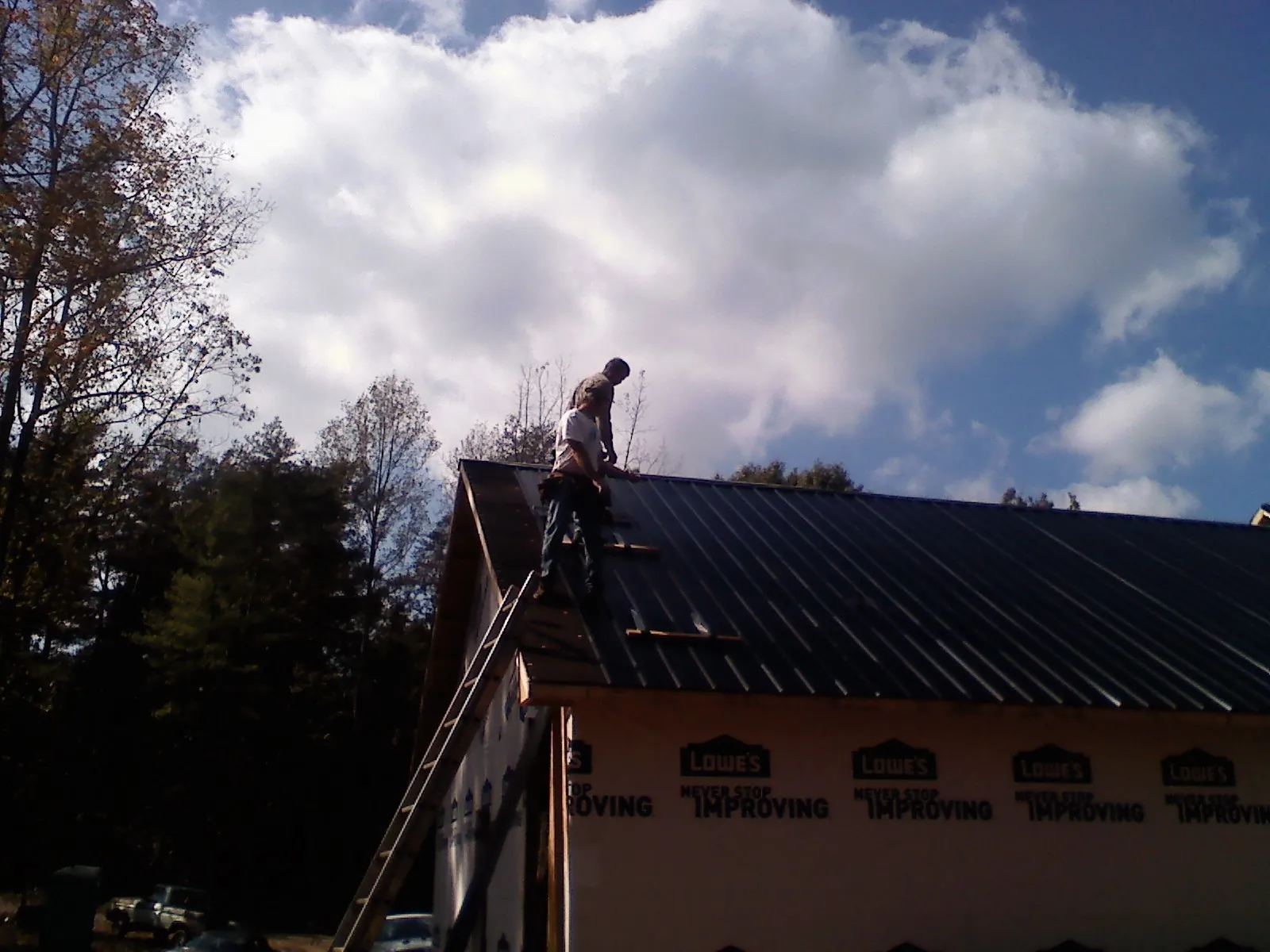 Roofer fastening dark metal panels high against a cloudy sky, from a Roof Inspection job in Bound Brook